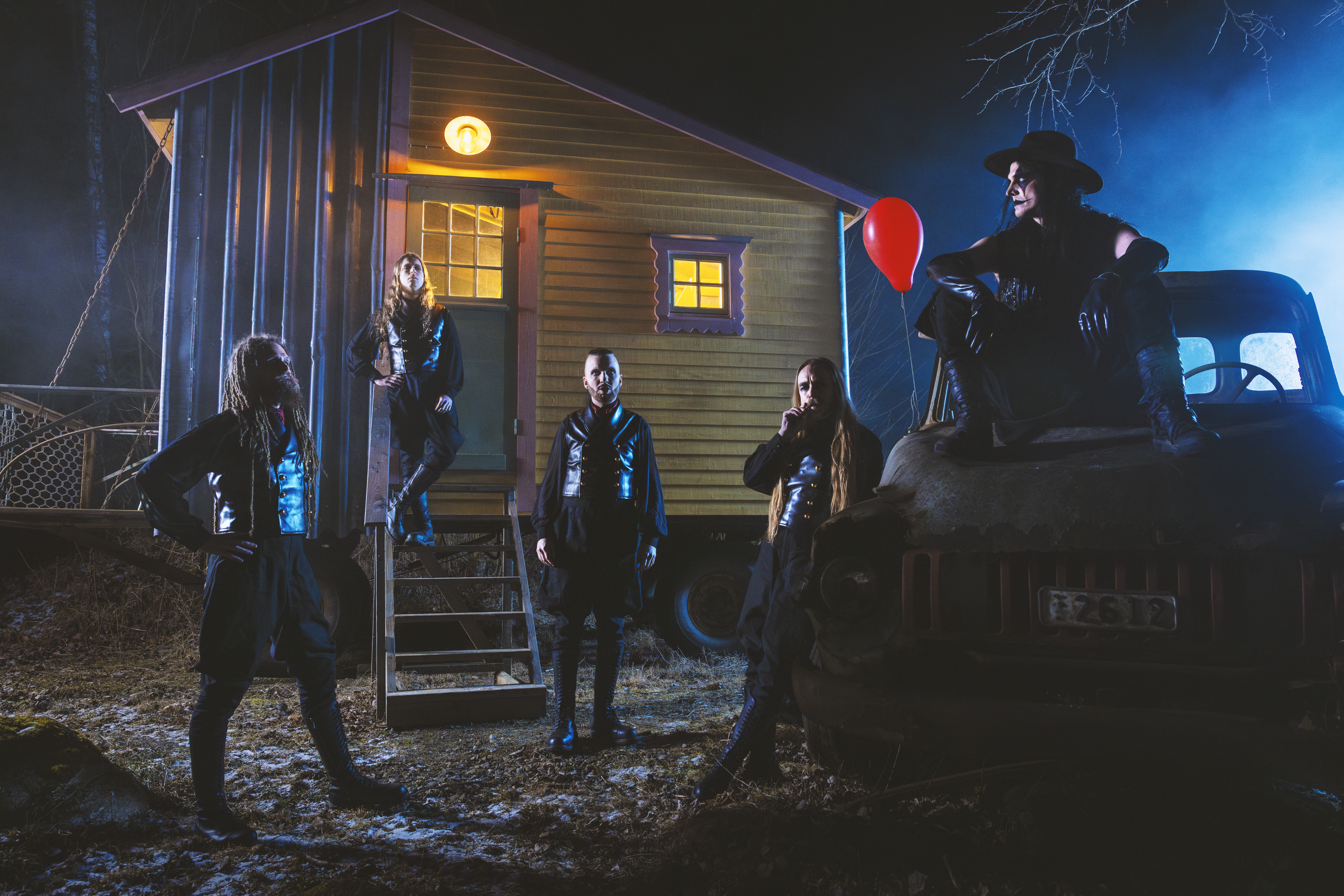 Members of Avatar in front of a cabin at night. The vocalist is sitting on an old truck and a red balloon is next to him.