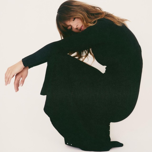 Melody wearing a black dress squatting in front of a white wall.