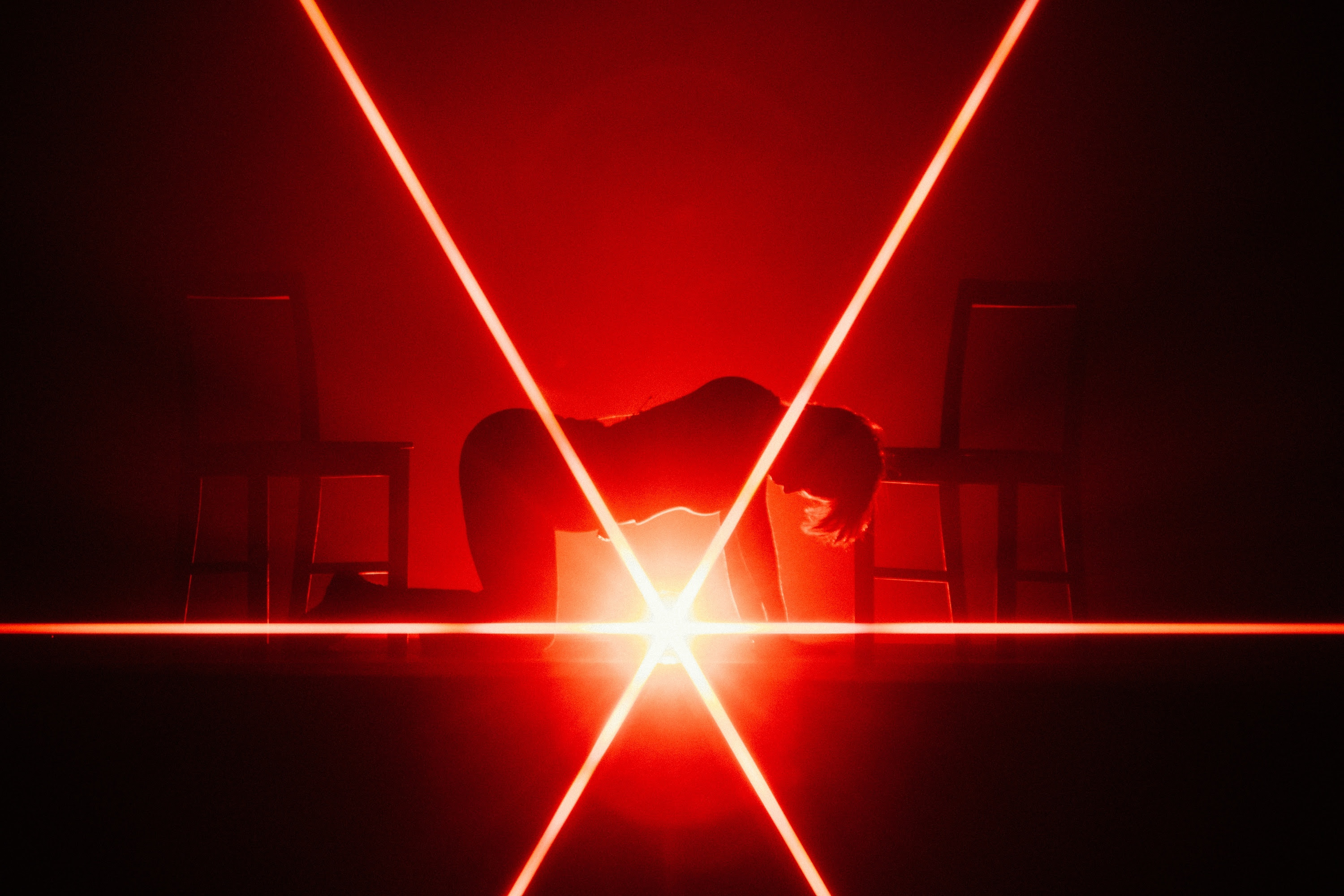 A silhouette of Mitski on all fours between two chains facing inwards with red lighting behind them.