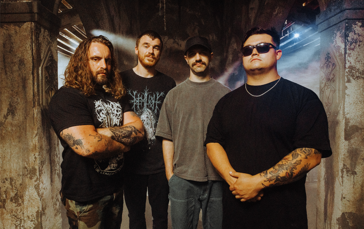 Band members standing in t-shirts facing camera with blank expressions.