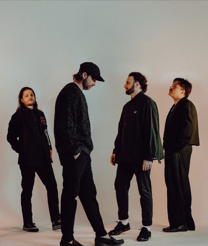 Band members dressed in black standing in front of a blank wall.