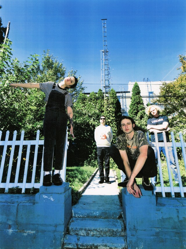 MX Lonely members standing outside in a vertical photo. Some members are sitting and standing in front of a white fence while the others stand behind it.