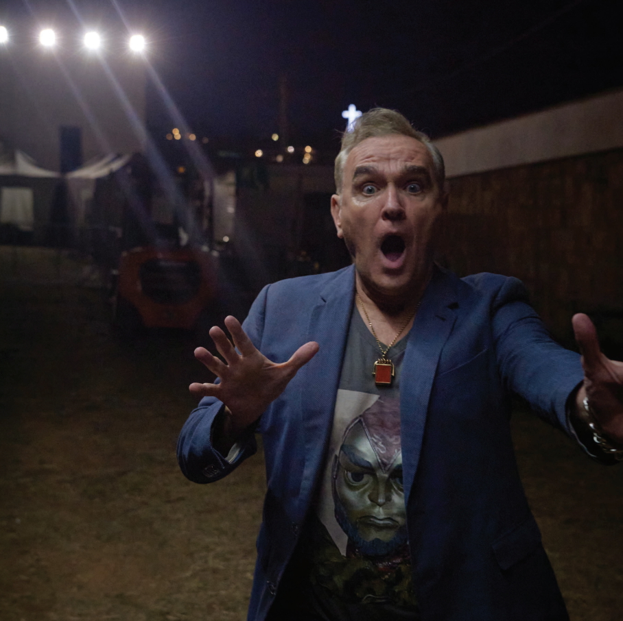 Morrissey looking at the camera with his mouth open and his hands at chest level.