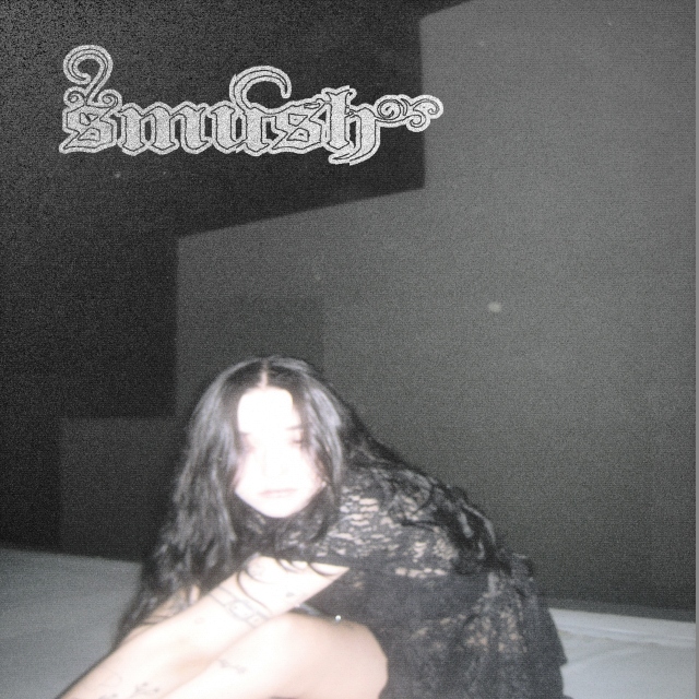 A high exposure photo of the lead singer sitting down wearing all black. "smush" is written in the upper left corner.