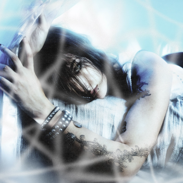 Forest laying on a bed facing the camera while holding a curtain.