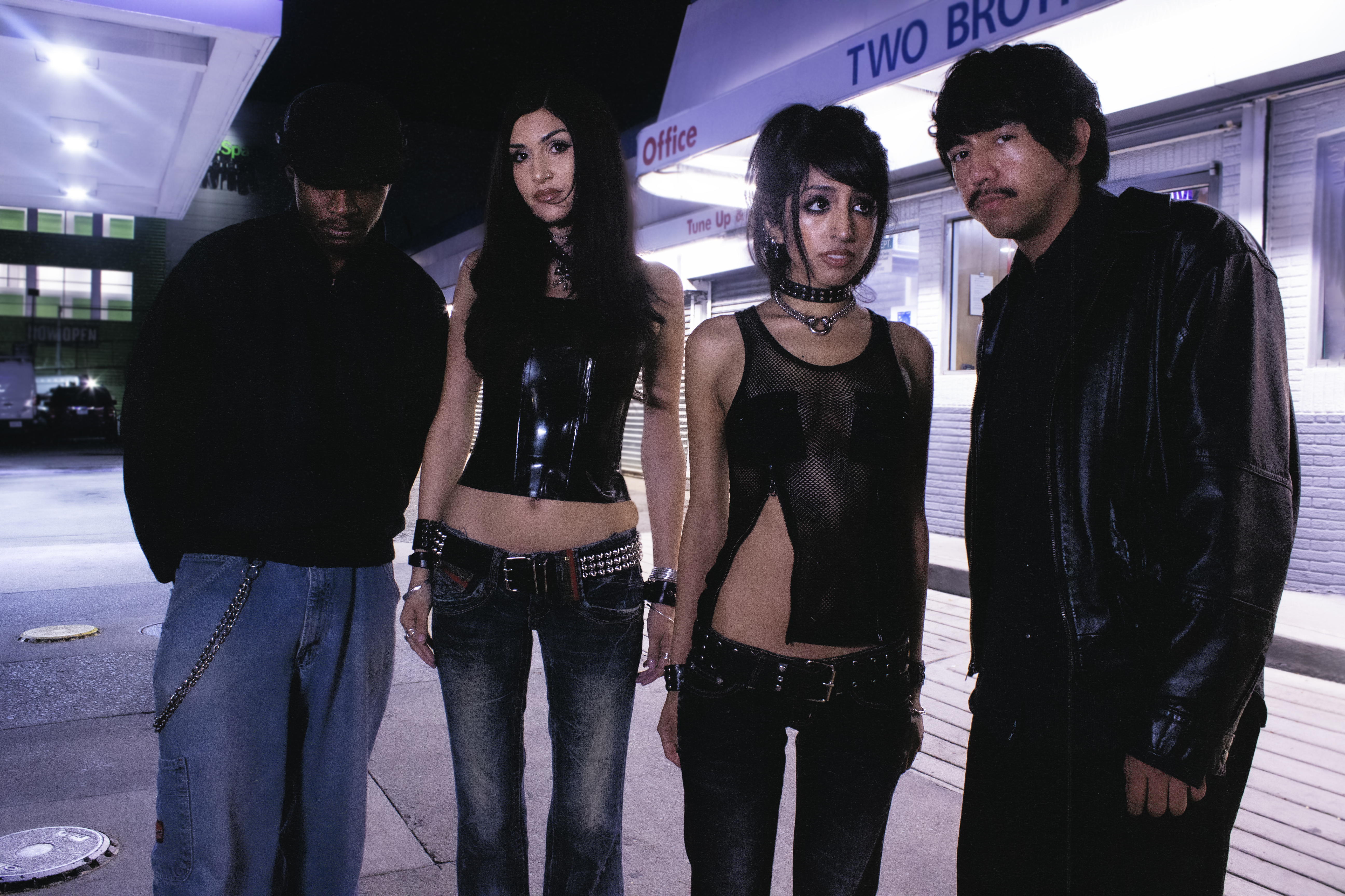 All four members of Glixen dressed in black standing in front of a store at night.