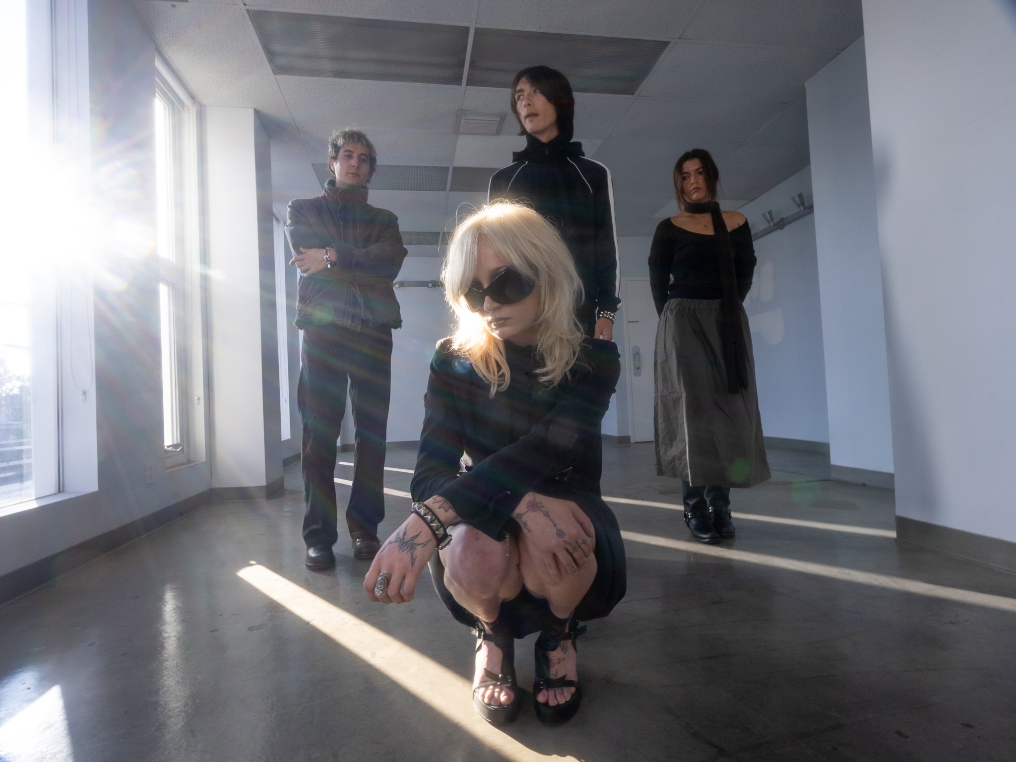 Hysteria members inside of an empty room. The vocalist is sitting close to the camera while the other band members stand behind.